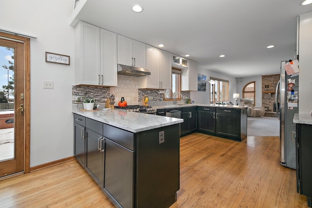 kitchen with a peninsula, under cabinet range hood, white cabinetry, and freestanding refrigerator