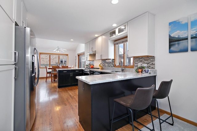 kitchen with stainless steel appliances, tasteful backsplash, white cabinetry, a sink, and a peninsula