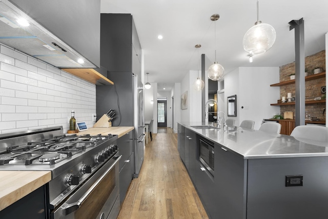 kitchen featuring light wood finished floors, gas stove, modern cabinets, dark cabinets, and wall chimney exhaust hood