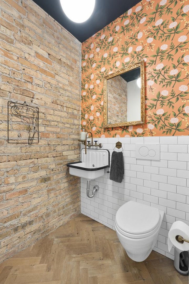 bathroom with toilet, wallpapered walls, a sink, and wainscoting