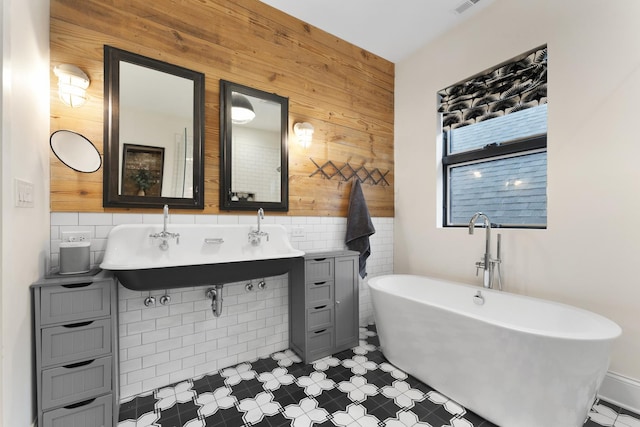 full bathroom with tile walls, a freestanding bath, wood walls, and a sink