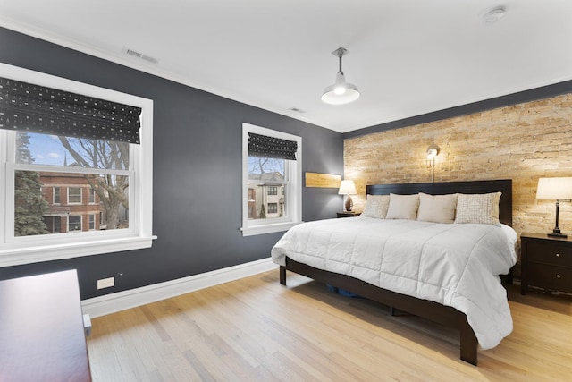 bedroom with ornamental molding, visible vents, baseboards, and wood finished floors