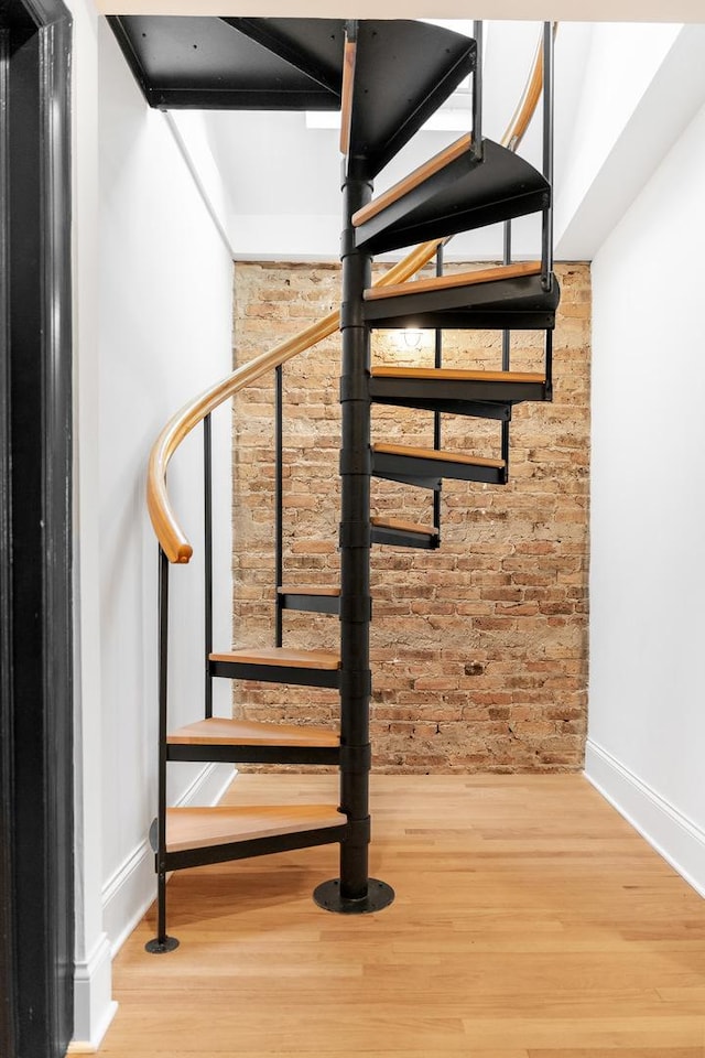 stairs featuring brick wall, wood finished floors, and baseboards