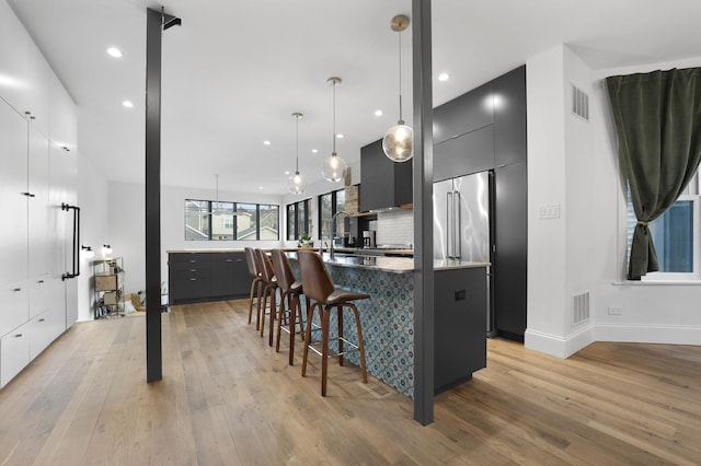 kitchen with light wood finished floors, tasteful backsplash, visible vents, a kitchen island with sink, and modern cabinets