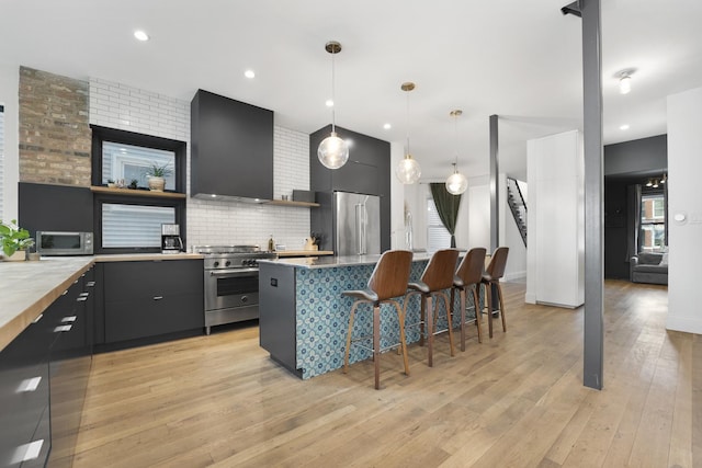 kitchen featuring light wood finished floors, high end appliances, a breakfast bar, a center island, and wall chimney range hood