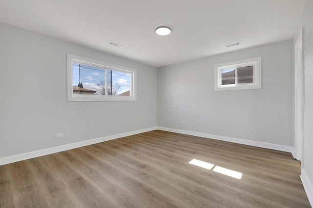 spare room with wood finished floors, visible vents, and baseboards