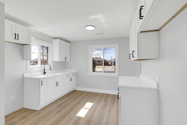 kitchen featuring light countertops, visible vents, light wood-style flooring, white cabinets, and a sink