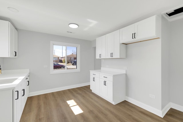 kitchen featuring light countertops, wood finished floors, white cabinetry, and baseboards