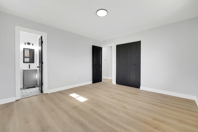 unfurnished bedroom featuring a closet, baseboards, light wood finished floors, and ensuite bathroom