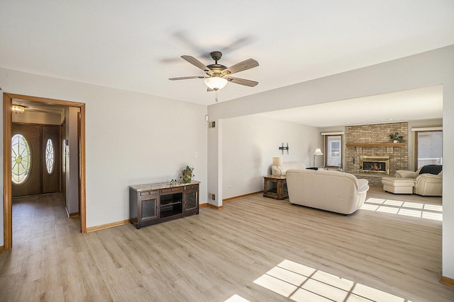 living room featuring light wood-type flooring, a brick fireplace, baseboards, and a ceiling fan