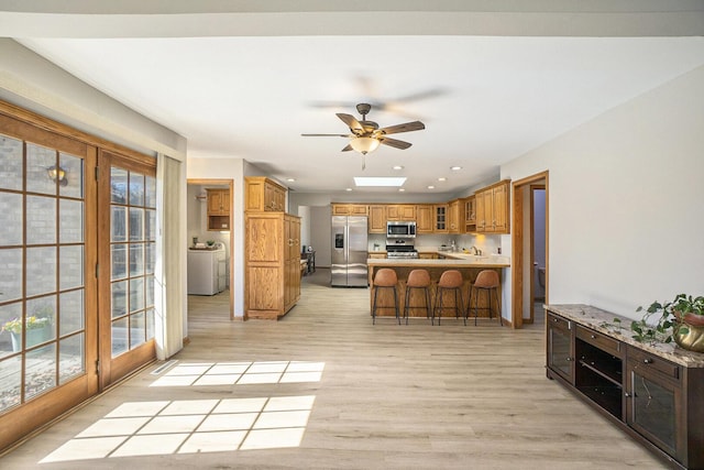 kitchen featuring a breakfast bar area, stainless steel appliances, a peninsula, light wood-type flooring, and washer / dryer