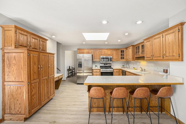 kitchen with a skylight, glass insert cabinets, a peninsula, stainless steel appliances, and a sink