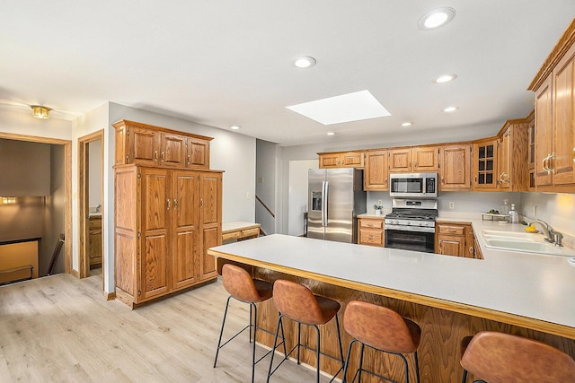 kitchen featuring a skylight, a sink, light countertops, appliances with stainless steel finishes, and light wood-type flooring