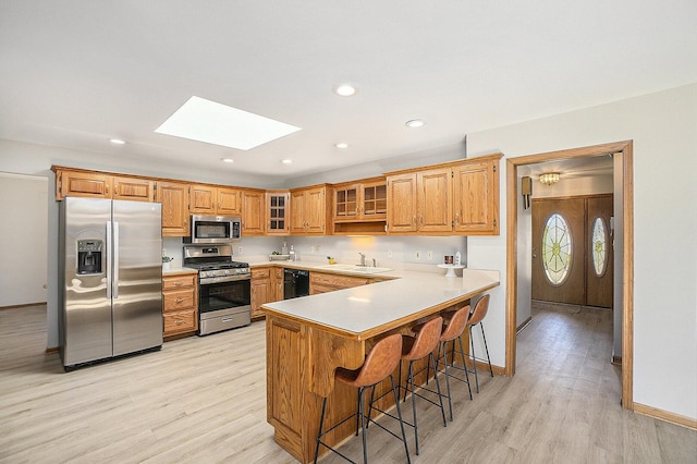 kitchen featuring stainless steel appliances, a sink, a peninsula, and light wood-style flooring