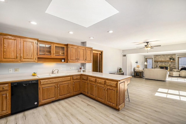 kitchen featuring black dishwasher, a peninsula, light countertops, a brick fireplace, and a sink