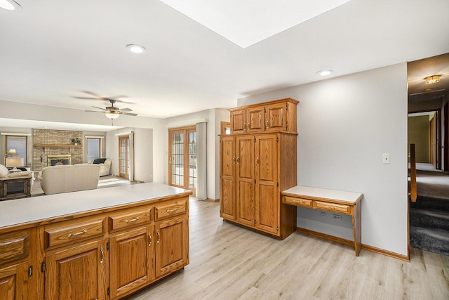 kitchen featuring a brick fireplace, light countertops, light wood-style floors, and brown cabinetry