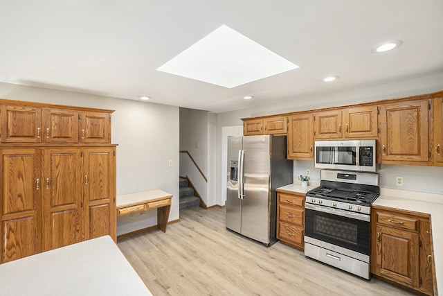 kitchen with a skylight, brown cabinets, stainless steel appliances, light countertops, and light wood-style floors