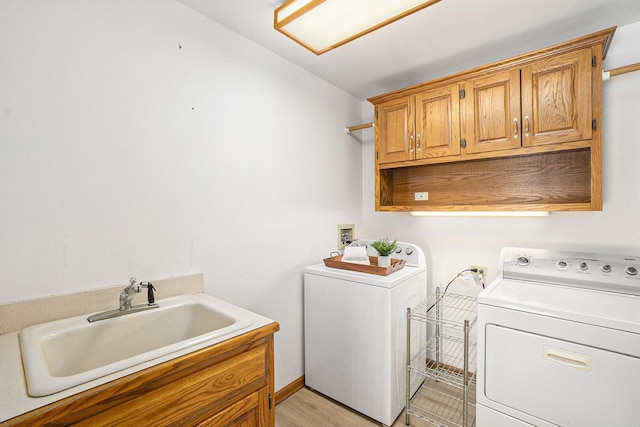 clothes washing area with light wood-type flooring, cabinet space, a sink, and washer and clothes dryer