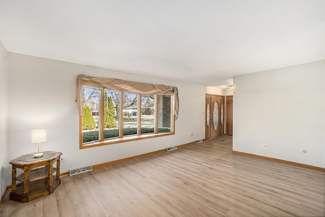 empty room with light wood-type flooring, visible vents, and baseboards