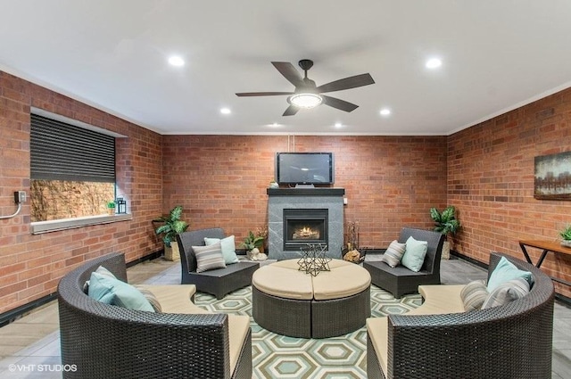 living room with a ceiling fan, recessed lighting, a warm lit fireplace, and brick wall