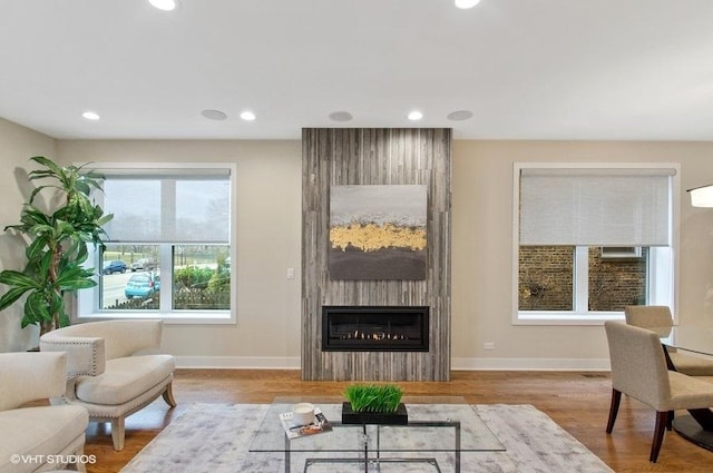 living room featuring a large fireplace, baseboards, wood finished floors, and recessed lighting