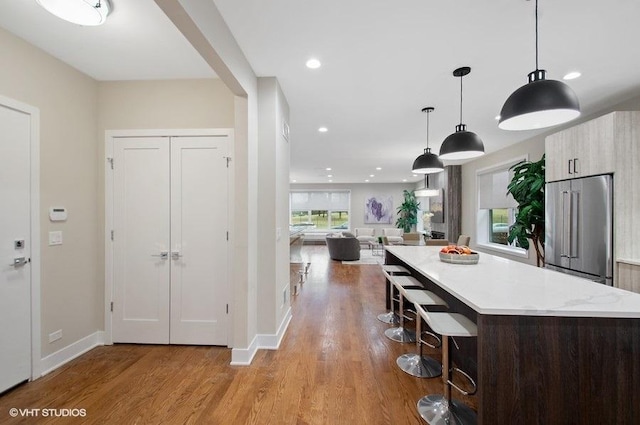 kitchen featuring light countertops, high quality fridge, a kitchen bar, and wood finished floors