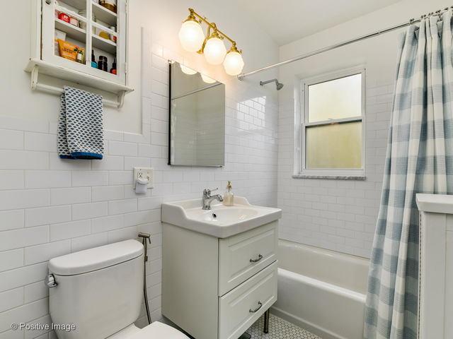 full bath featuring toilet, shower / tub combo, tile walls, and vanity