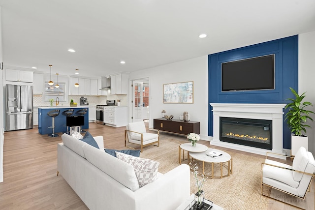 living area with light wood-type flooring, a glass covered fireplace, and recessed lighting