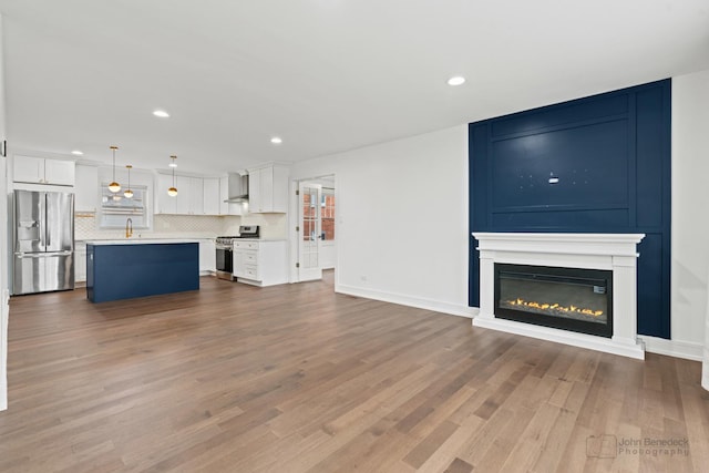 unfurnished living room featuring a large fireplace, baseboards, wood finished floors, and recessed lighting