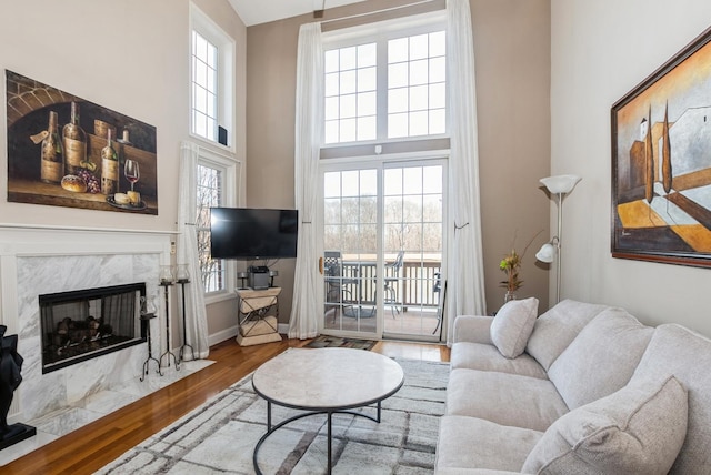 living room with a wealth of natural light, a premium fireplace, wood finished floors, and a towering ceiling