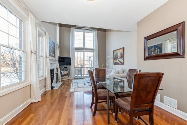 dining room featuring visible vents, a fireplace with flush hearth, baseboards, and wood finished floors