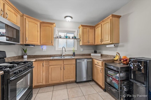 kitchen with dark countertops, light brown cabinetry, appliances with stainless steel finishes, light tile patterned flooring, and a sink