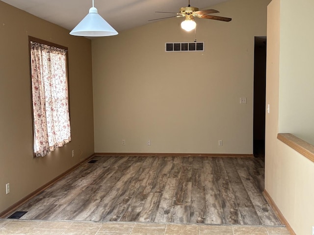 spare room featuring a ceiling fan, visible vents, baseboards, and wood finished floors