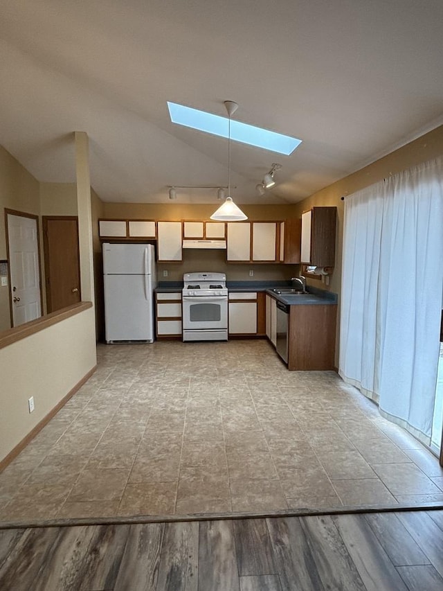 kitchen featuring vaulted ceiling with skylight, white appliances, a sink, hanging light fixtures, and dark countertops