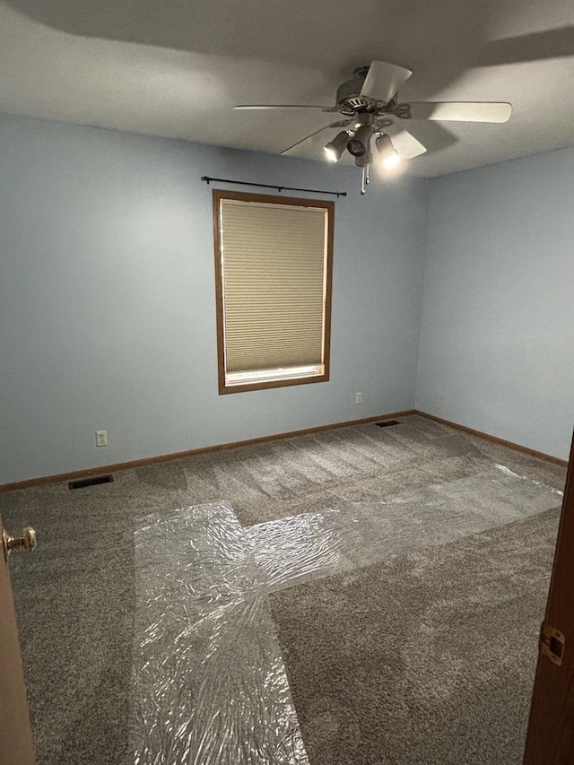 carpeted spare room featuring a ceiling fan, visible vents, and baseboards