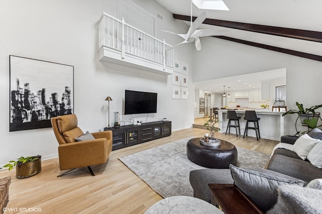 living area with high vaulted ceiling, a skylight, baseboards, light wood finished floors, and beamed ceiling