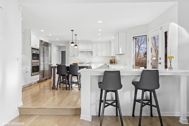 kitchen with backsplash, appliances with stainless steel finishes, white cabinetry, light wood-type flooring, and a kitchen breakfast bar