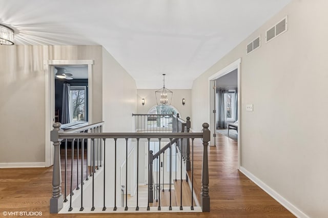 hallway with visible vents, wood finished floors, an upstairs landing, and a notable chandelier