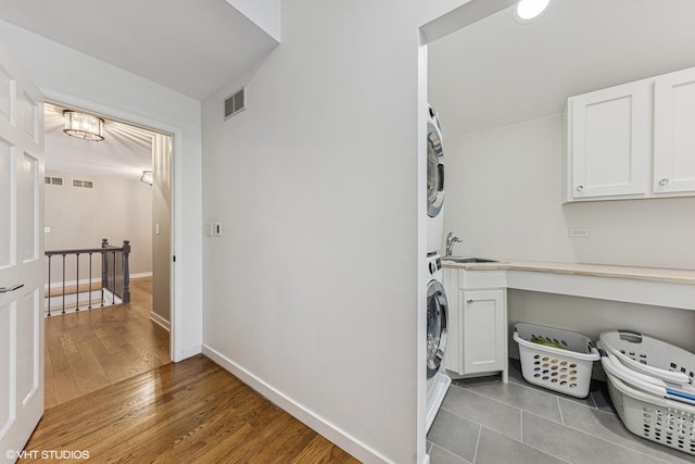 washroom featuring stacked washer / dryer, a sink, visible vents, baseboards, and cabinet space