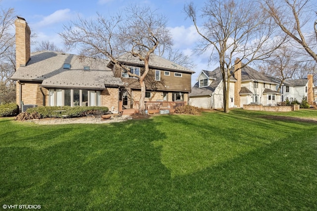 back of house featuring brick siding, a lawn, a wooden deck, a chimney, and a high end roof