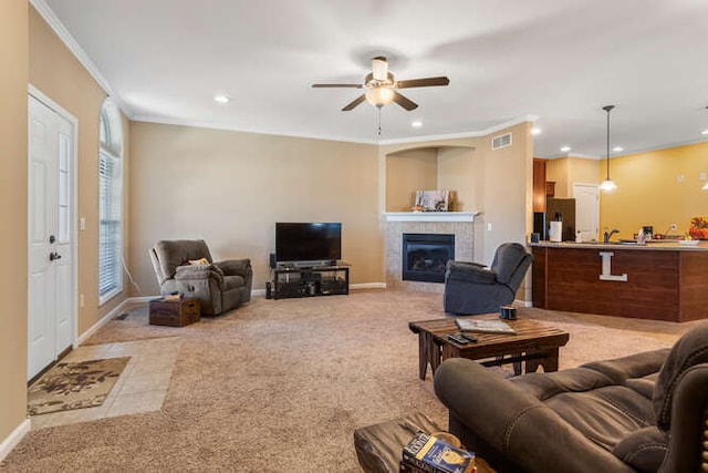 living room with visible vents, baseboards, a tiled fireplace, crown molding, and light colored carpet