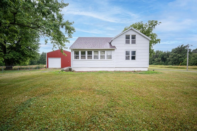 back of property with roof with shingles, a detached garage, an outdoor structure, and a yard