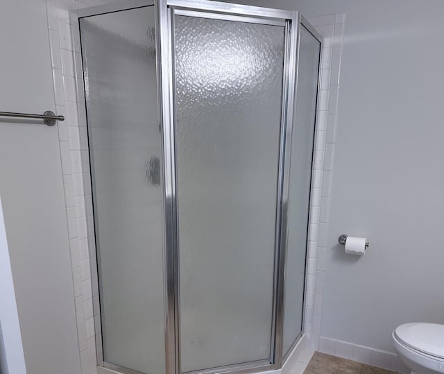 bathroom with tile patterned flooring, a shower stall, toilet, and baseboards