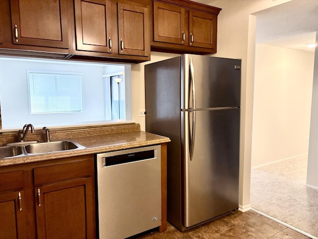 kitchen with brown cabinetry, stainless steel appliances, a sink, and dark colored carpet