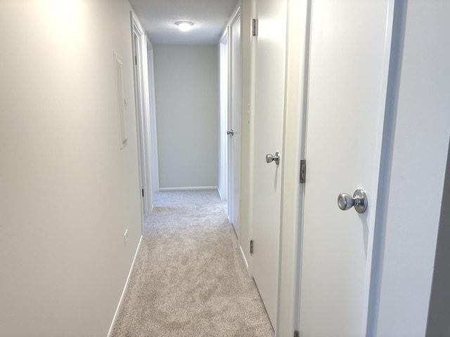 corridor with baseboards and light colored carpet