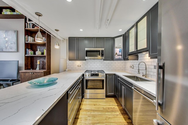 kitchen with light stone countertops, pendant lighting, light wood-type flooring, appliances with stainless steel finishes, and a sink