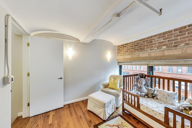 living area with wood finished floors, baseboards, and brick wall