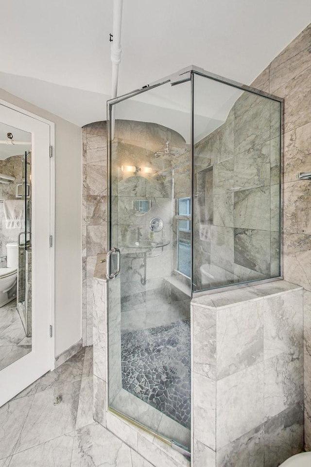 bathroom featuring toilet, marble finish floor, and a shower stall