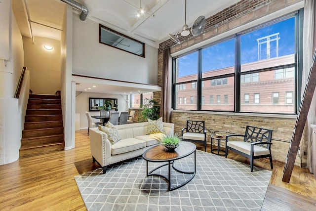 living area featuring brick wall, stairs, a towering ceiling, and wood finished floors