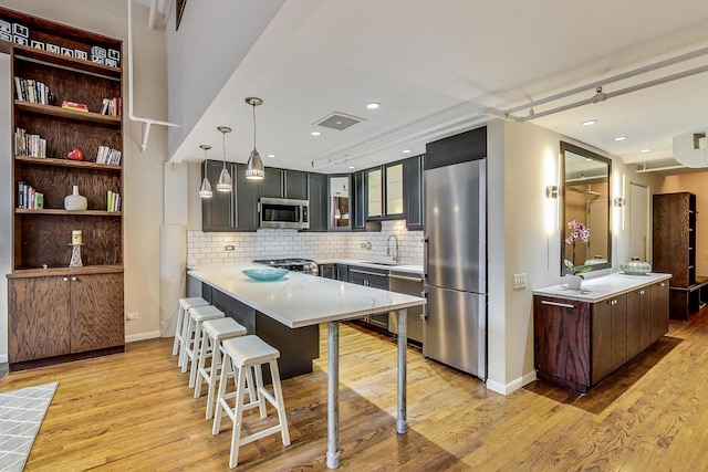 kitchen featuring visible vents, a breakfast bar, a sink, a peninsula, and appliances with stainless steel finishes